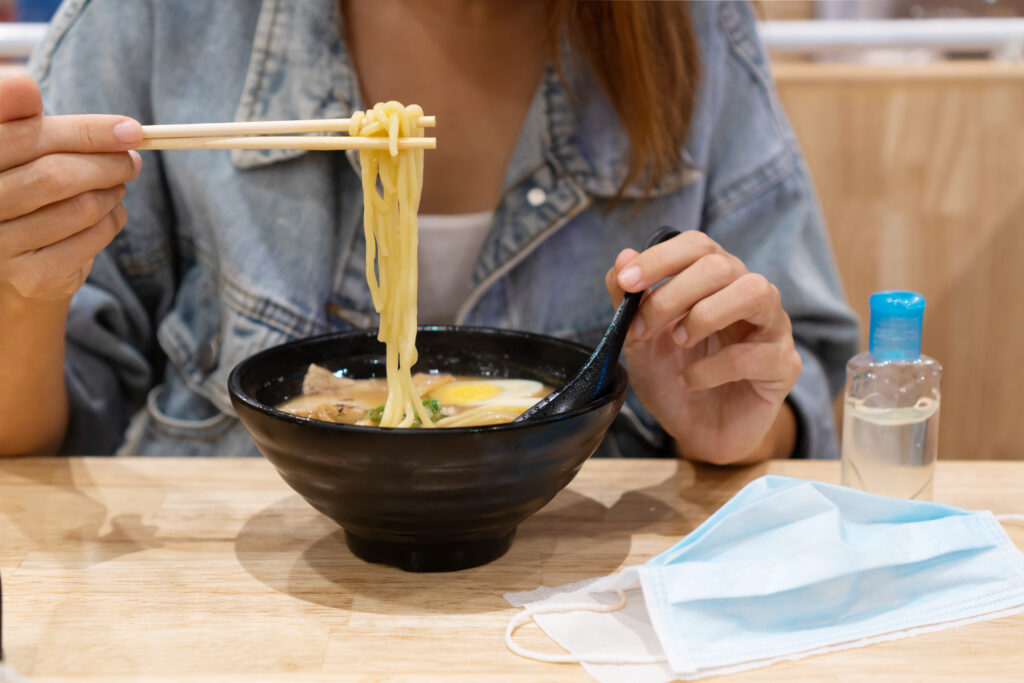 Young asian girl eating ramen with sanitizer gel and surgical fa