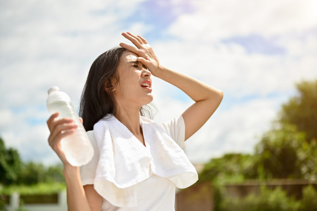 An exhausted asian woman is fighting the heat wave while running in a park on a sunny day.